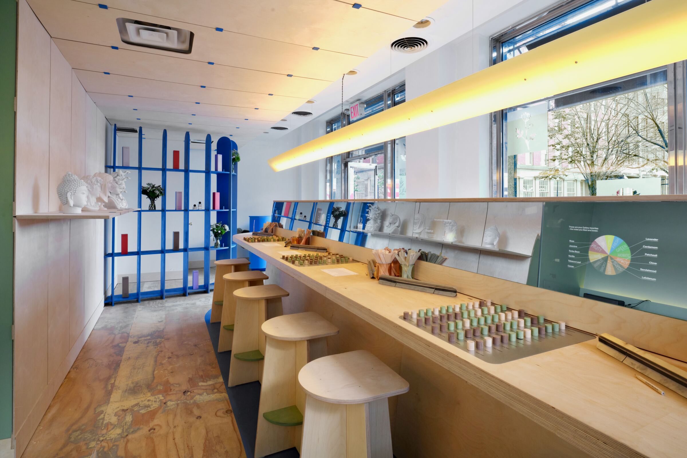 The Fragrance Studio’s long plywood bench with note trays set into the top, a row of stools and blue display shelves beyond