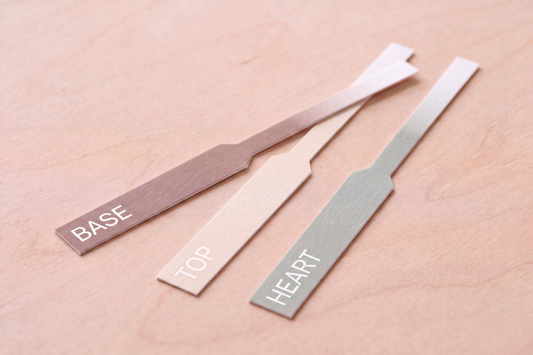 Three printed scent strips labeled Base, Top and Heart on a maple bench