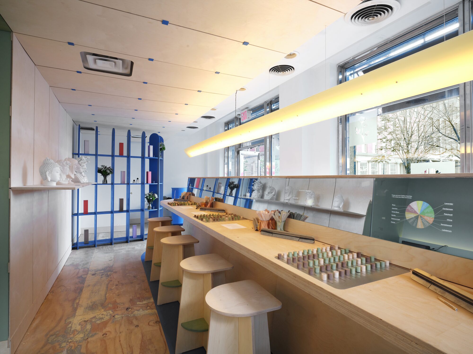 The Fragrance Studio’s long plywood bench with trays of note samples set into the top, a row of stools and blue display shelves beyond